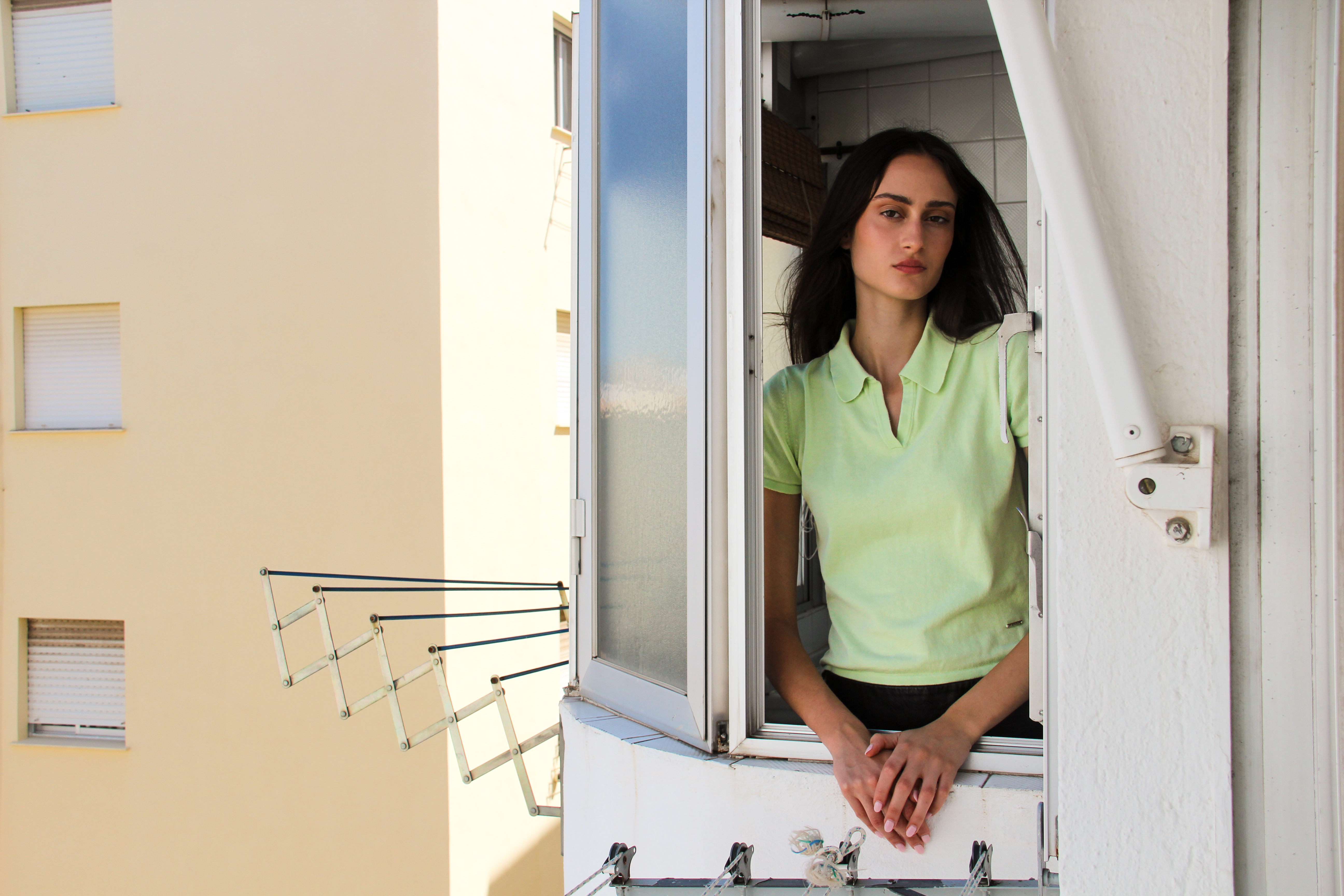 Modelo asomándose por la ventana del área de lavandería hacia el exterior, en una escena cotidiana de la editorial “Grangran’s”